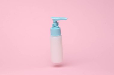 Cream dispenser bottle flying in antigravity on pink background with shadow. Levitation object in the air. Beauty and fashion concept. Creative minimal layout