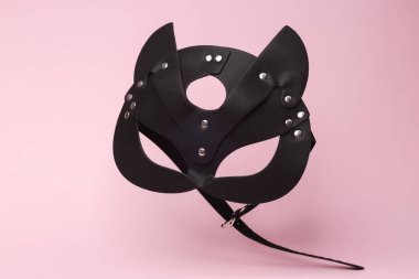 Bdsm leather cat mask flying in antigravity on pink background with shadow. Levitation object in the air. Sex game concept. Creative minimal layout