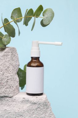 Treatment of sore throat. Throat spray on stone with sprig of eucalyptus on a blue background. Medicine still life