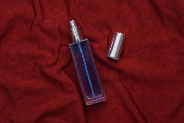 Glass bottle of perfume on red crumpled silk background