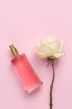 Pembe arka planda gül olan parfüm şişesi.