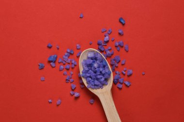 Kırmızı arka planda banyo tuzu olan ahşap kaşık.