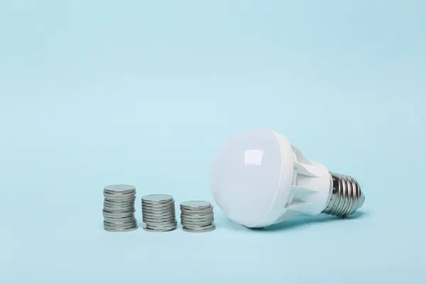 Saving money concept. Energy saving led light bulb with a stack of coins on a blue background