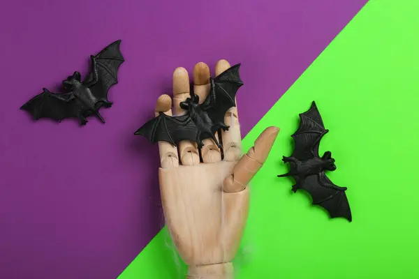 Halloween minimal still life. Wooden hand with bats on purple green background. Top view