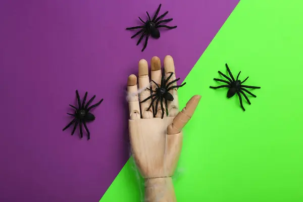 Halloween minimal still life. Wooden hand with spiders on purple green background. Top view
