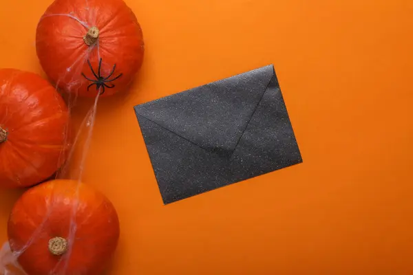 Halloween background. Black envelope and pumpkins in web with spider on orange background. Happy Halloween