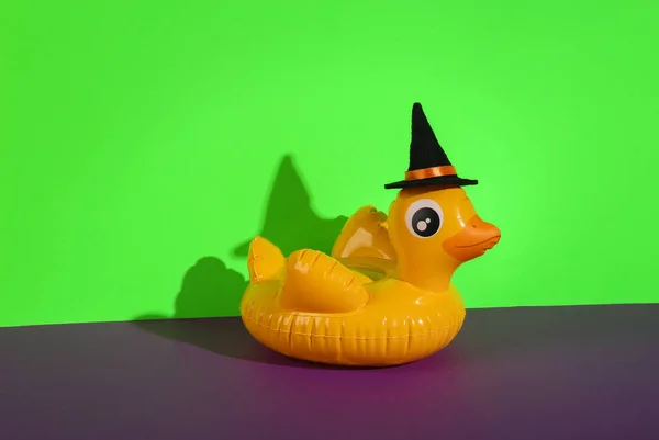 Halloween still life of inflatable duck with witch hat on green purple background