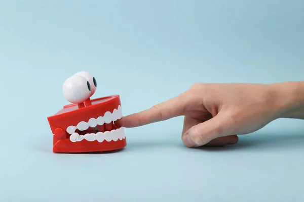 Funny toy clockwork jumping teeth with eyes biting finger of hand, blue background.