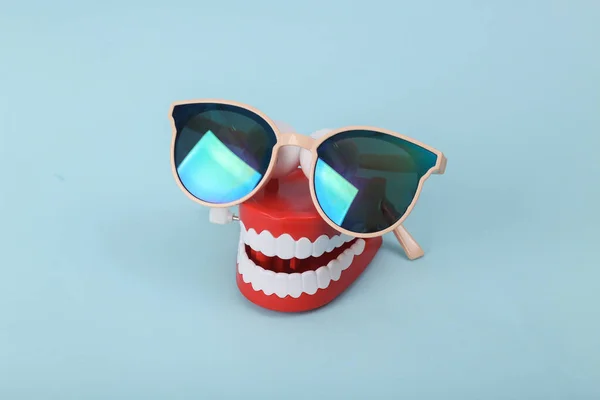 Funny toy clockwork jumping teeth with sunglasses on blue background.