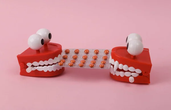 Two Funny  clockwork jumping teeth toy with pills on pink background.