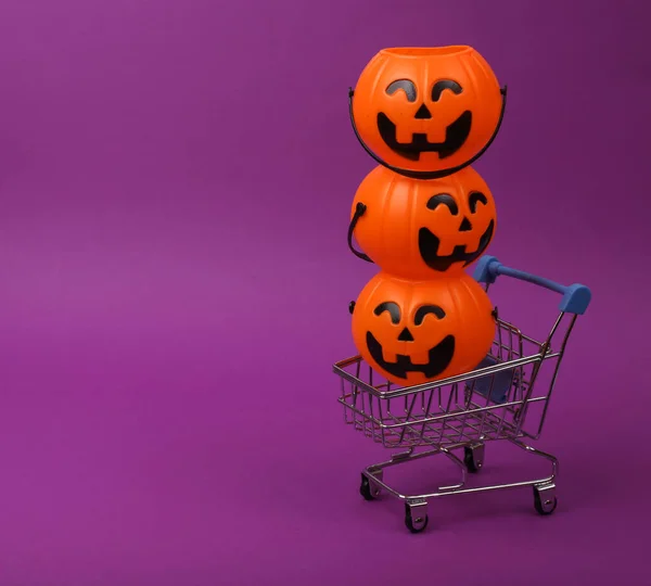 Mini supermarket cart with halloween candy buckets on purple background