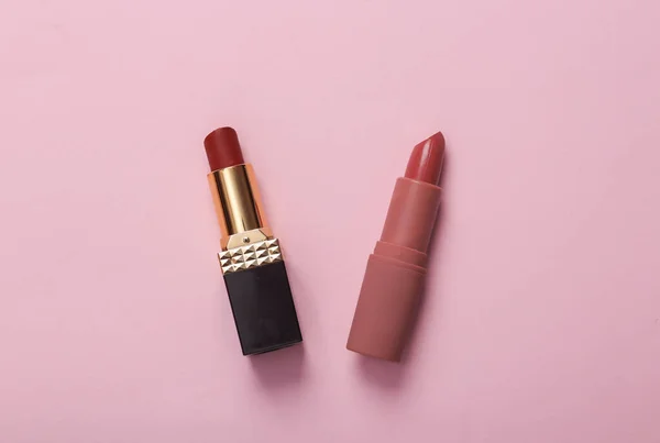 Two tubes of different lipsticks on a pink background