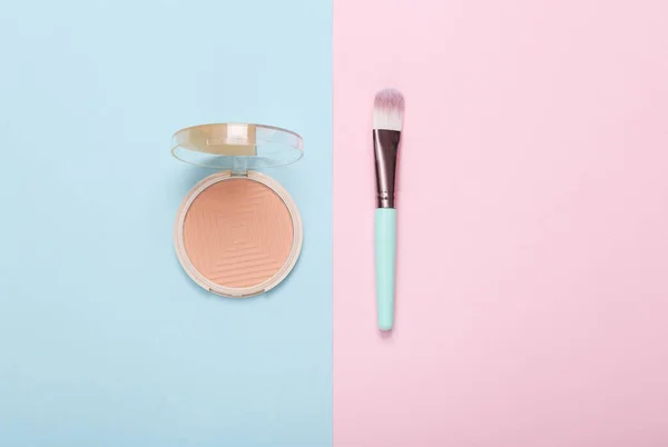 Make-up powder box and brush on a blue-pink background. Top view