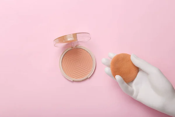 Plastic hand holding Make-up powder box on pink background. Top view