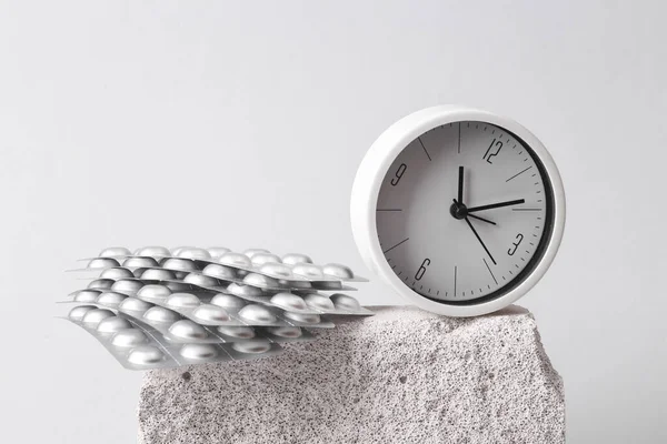 Round Clock with pills blister on stone, gray background. Minimal composition