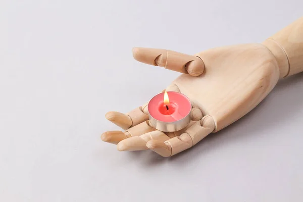Wooden puppet hand with flaming candle on a gray background