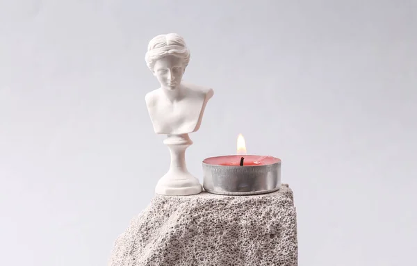 Minimalistic aesthetic still life of Venus bust and flaming candle on stone