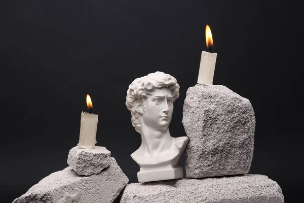 Flaming candles with David bust on stone. Black background. Modern still life. Aesthetic minimalist composition.