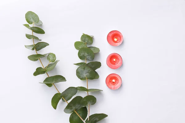Flaming aroma candles with eucalyptus branches on white background. Aroma therapy. Top view