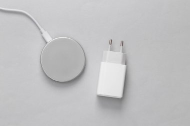 Gadgets evrimi. Kablosuz şarj platformu ve gri arka planda eski şarj adaptörü. Üst görünüm