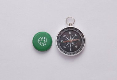 Dairesel geri dönüşüm sembollü plastik şişe kapağı ve gri arka planda pusula. Geri dönüşüm kavramı