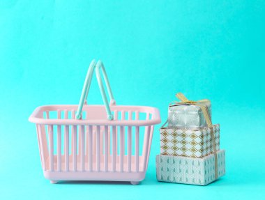 Turkuaz bir arka planda süpermarket sepetine sarılı noel hediyesi kutuları.