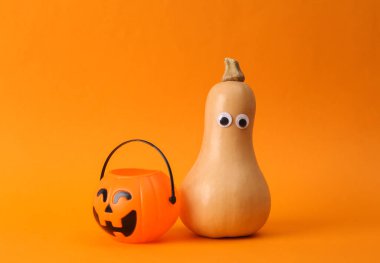 Minimalist cadılar bayramı natürmortu. Turuncu arka planda cadılar bayramı kovası olan bir balkabağı. Şeker mi şaka mı?