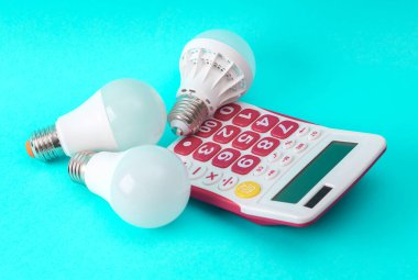 Elektrik maliyetleri, tasarruf konsepti, enerji tasarrufu ve modern ampullerin enerji tüketimi. Mavi arkaplanda ampulleri olan hesap makinesi
