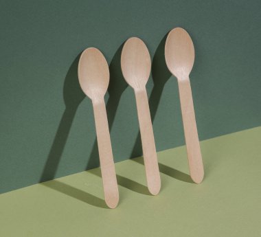 Minimalist eko natürmort. Tahta kaşıklar, gölgeli yeşil iki tonlu arka plan üzerine kurulmuş. Yaratıcı kompozisyon. Yiyecek ve içecek.