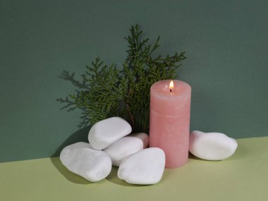 Aesthetic minimal still life. natural concept. Flaming aroma candle with pebbles and a sprig of eucalyptus on a green two-tone background