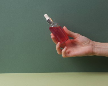 Hand holds serum bottle on green background. Beauty concept.