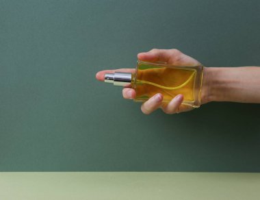 Female Hand holds perfume bottle on green background. Beauty concept.