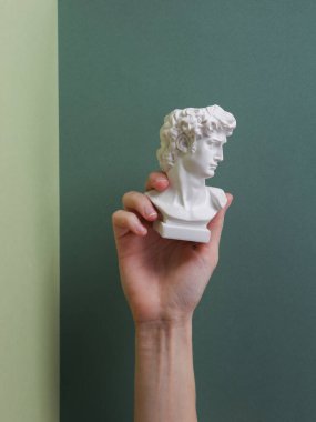 Hand holding antique David statue on green background