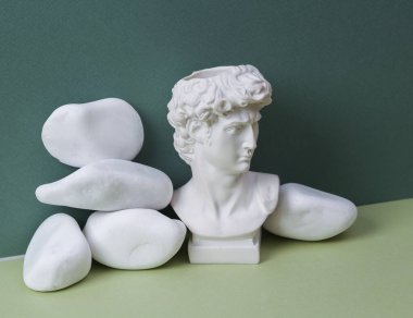 Aesthetic minimalistic still life. Antique David statue and pebbles on green background