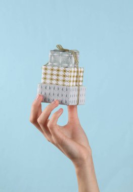 Stack of Christmas gift boxes in female hand on blue background.