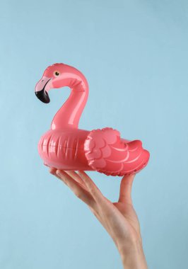 Miniature rubber inflatable pink flamingo in female hand on a blue background.