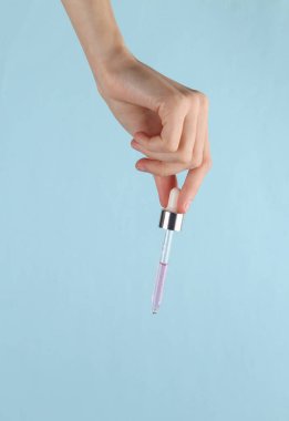 Facial serum dropper in female hand on a blue background. Beauty concept