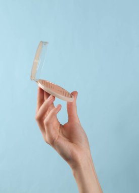 Makeup powder box in female hand on blue background.
