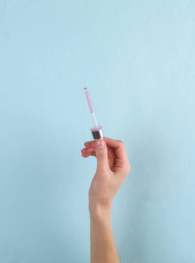 Facial serum dropper in female hand on a blue background. Beauty concept