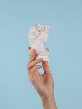 Antique David bust in female hand on a blue background.