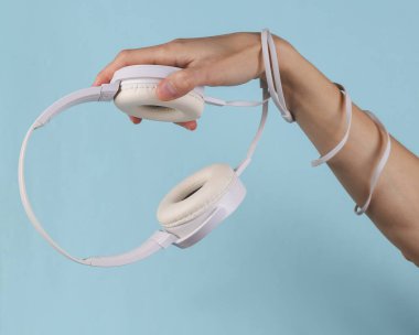 White stereo headpgones in female hand on a blue background.