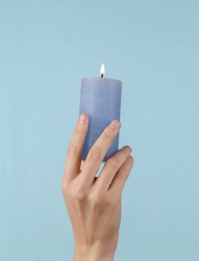 Flaming aroma candle in female hand on a blue background