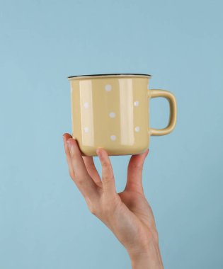 Ceramic cup in female hand on blue background