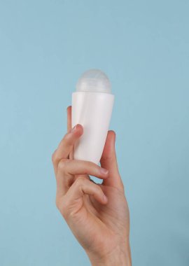 Antiperspirant roll-on stick in female hand on a blue background