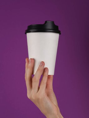 Take away white coffee cup in female hand on a purple background.