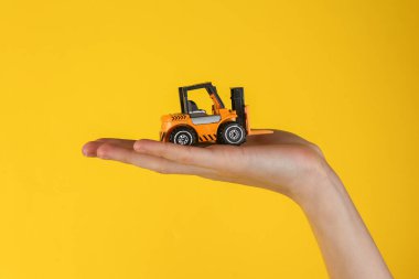 Mini model yellow taxi car in female hand on yellow background.