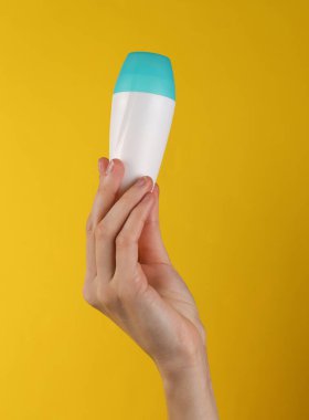 Antiperspirant roll-on stick in female hand on yellow background