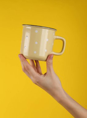 Ceramic yellow cup in female hand on yellow background