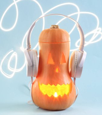 Glowing Halloween pumpkin with stereo headphones on blue bright background. Scary glowing face, sinister smile. Minimal halloween or music concept. Trick or Treat