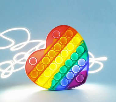 Pop it antistress heart shaped toy on blue bright backgroud with light effect
